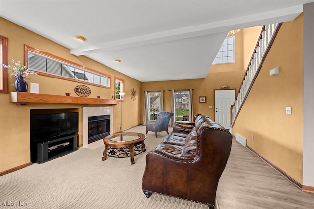 living area featuring visible vents, beamed ceiling, baseboards, stairway, and a tile fireplace