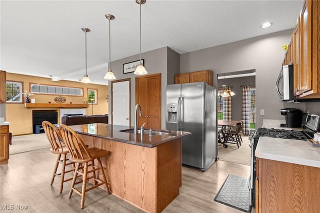 kitchen with brown cabinetry, a kitchen bar, a center island with sink, a sink, and stainless steel appliances