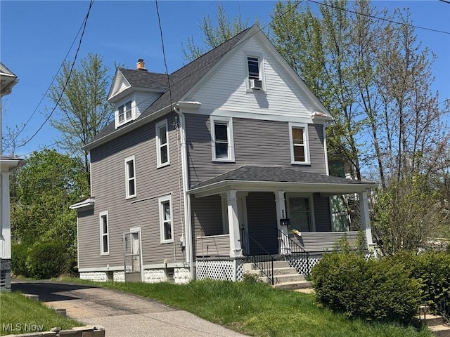 view of front facade featuring roof with shingles, a chimney, cooling unit, and a porch