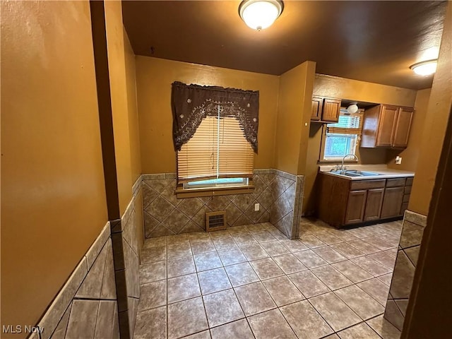 kitchen with brown cabinetry, light countertops, a sink, visible vents, and light tile patterned flooring