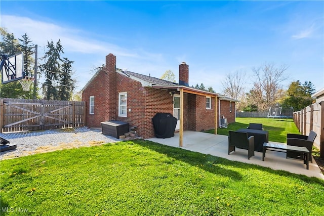 rear view of property with a chimney, a trampoline, a fenced backyard, a yard, and a patio area