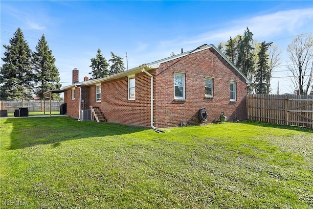 view of side of home with a chimney, a fenced backyard, brick siding, central AC unit, and a lawn