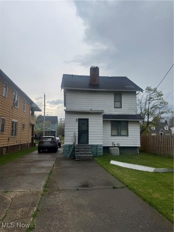 view of front of home featuring fence, a front yard, entry steps, a chimney, and concrete driveway