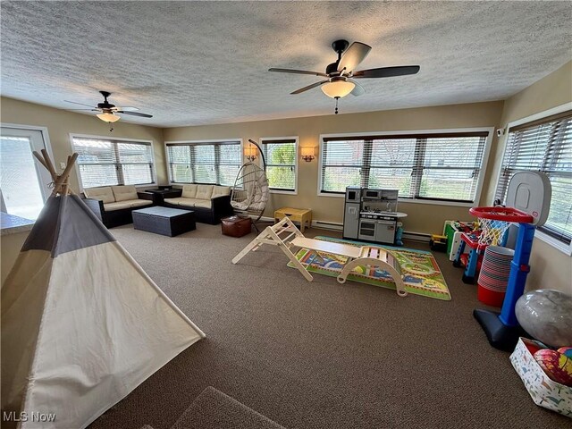 playroom with a baseboard heating unit, a textured ceiling, ceiling fan, and carpet