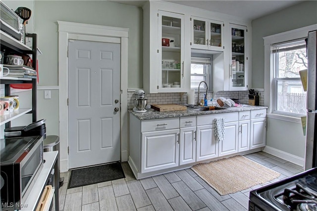 kitchen featuring white cabinetry, decorative backsplash, glass insert cabinets, and a sink