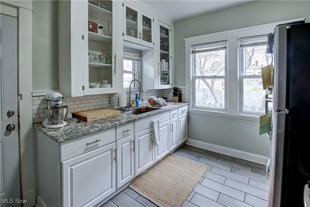 kitchen featuring a sink, glass insert cabinets, backsplash, white cabinetry, and freestanding refrigerator
