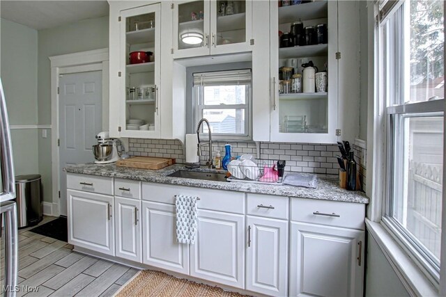 kitchen featuring decorative backsplash, white cabinets, glass insert cabinets, and a sink