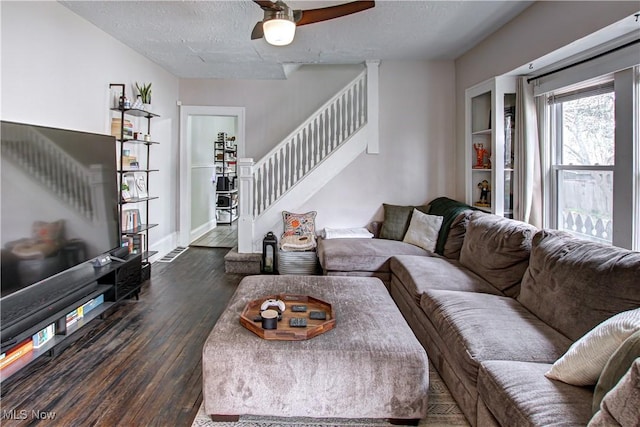 living area with a ceiling fan, dark wood-style flooring, stairway, and a textured ceiling