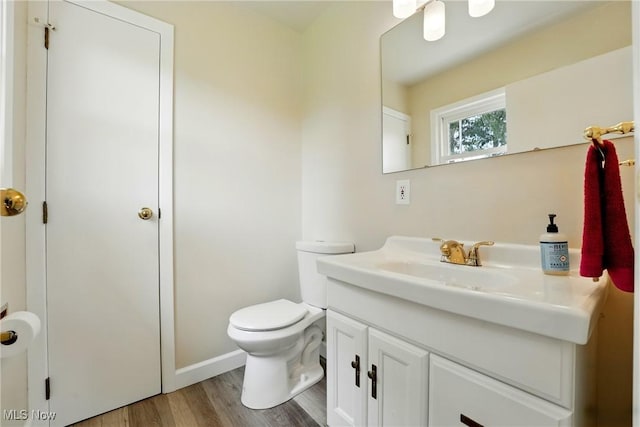half bath with wood finished floors, vanity, toilet, and baseboards