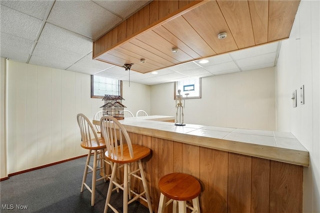 bar with wet bar, dark carpet, a healthy amount of sunlight, and a paneled ceiling