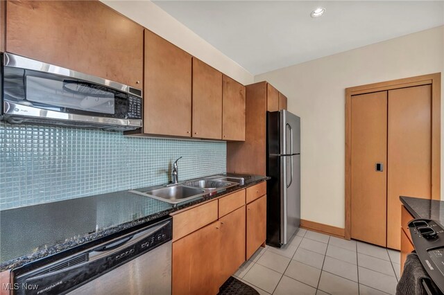 kitchen featuring decorative backsplash, appliances with stainless steel finishes, dark countertops, a sink, and light tile patterned flooring