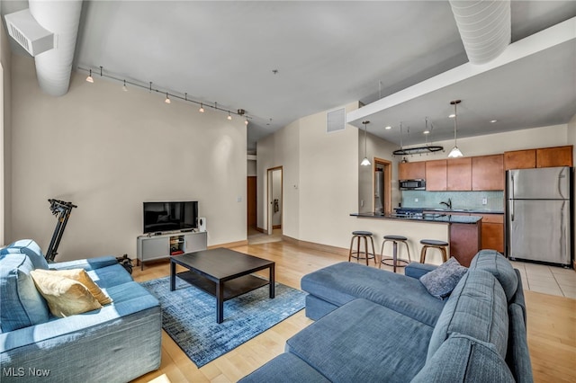 living area featuring baseboards, visible vents, light wood-type flooring, and rail lighting