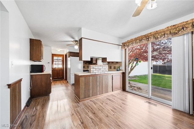 kitchen featuring ceiling fan, visible vents, freestanding refrigerator, a peninsula, and light wood-style floors