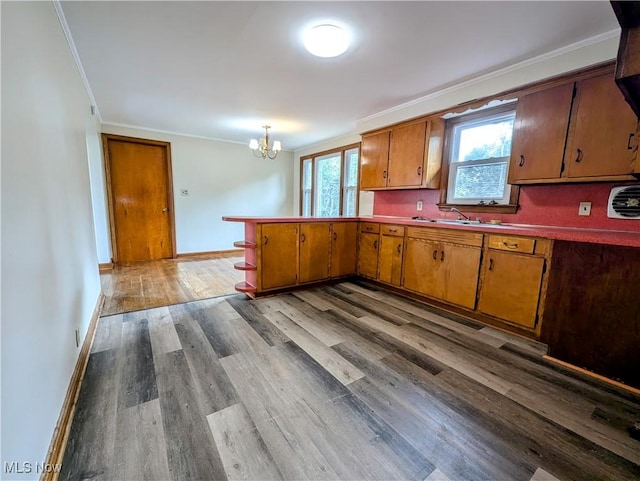 kitchen featuring brown cabinets, a notable chandelier, dark wood-type flooring, a peninsula, and ornamental molding