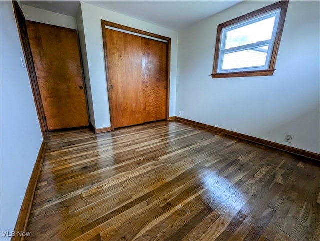 unfurnished bedroom featuring dark wood-style floors, baseboards, and a closet