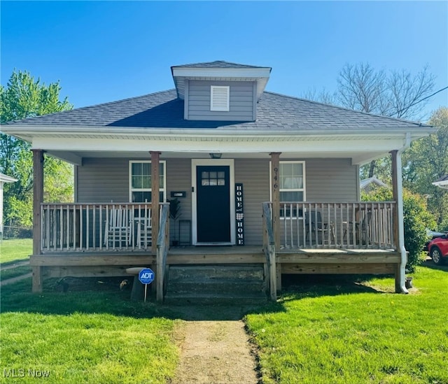 bungalow-style home featuring roof with shingles, covered porch, and a front yard