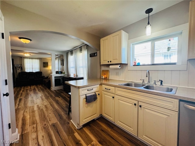 kitchen with a sink, dark wood-type flooring, a peninsula, arched walkways, and dishwasher