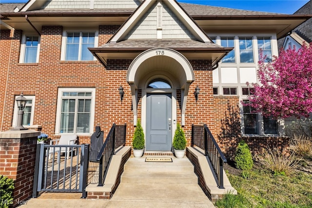 entrance to property with a shingled roof and brick siding