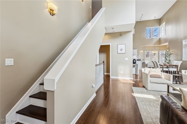 living area with a towering ceiling, hardwood / wood-style floors, baseboards, and stairs