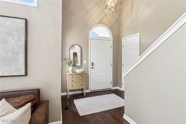 entryway with dark wood-style floors, baseboards, a notable chandelier, and a high ceiling