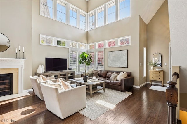 living room with a towering ceiling, dark wood-style flooring, baseboards, and a glass covered fireplace