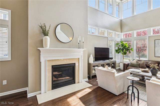living room with dark wood-style flooring, a high ceiling, a high end fireplace, and baseboards