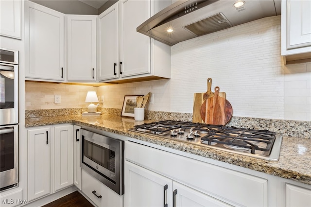 kitchen with wall chimney range hood, white cabinetry, stainless steel appliances, and backsplash