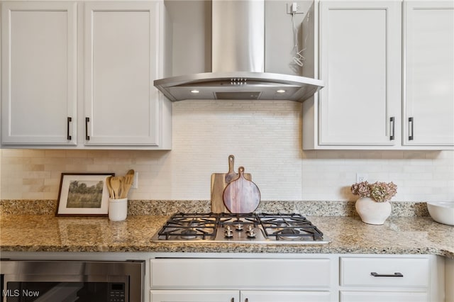 kitchen featuring light stone counters, decorative backsplash, appliances with stainless steel finishes, white cabinetry, and wall chimney exhaust hood