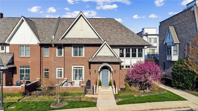 view of property featuring a shingled roof and brick siding