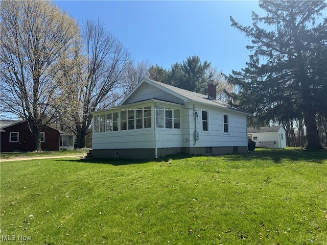 exterior space with a chimney, a storage unit, an outbuilding, a sunroom, and a front yard