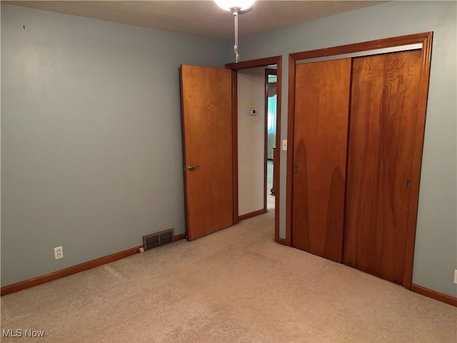 unfurnished bedroom with a closet, visible vents, light colored carpet, and baseboards