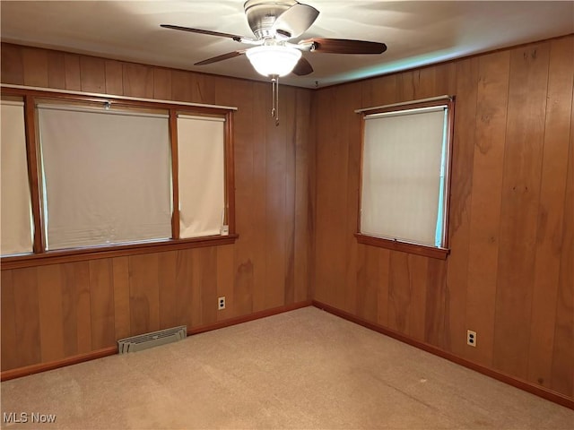carpeted empty room with wooden walls, visible vents, ceiling fan, and baseboards