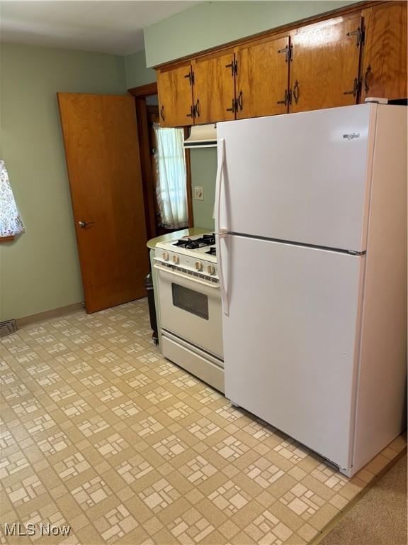 kitchen with baseboards, brown cabinetry, and white appliances