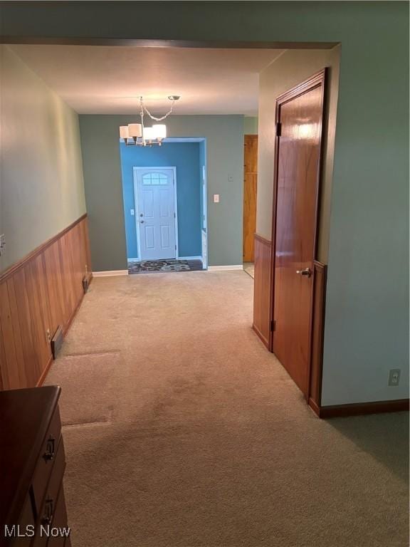corridor featuring baseboards, wainscoting, light carpet, and an inviting chandelier