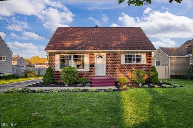 cape cod home featuring a front lawn, roof with shingles, brick siding, and fence
