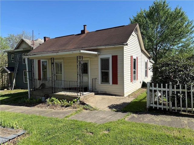 view of front facade featuring a front lawn, covered porch, and a chimney