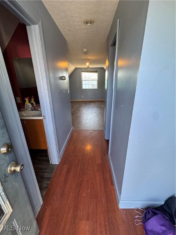 corridor with a textured ceiling, wood finished floors, and baseboards