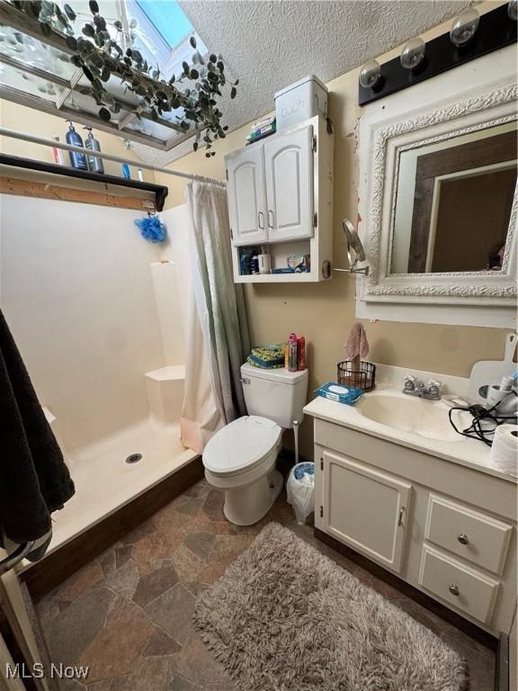 full bath with a shower stall, vanity, stone finish flooring, toilet, and a textured ceiling