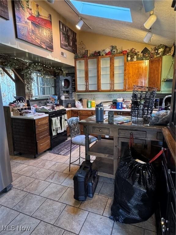 kitchen featuring lofted ceiling with skylight, brown cabinetry, glass insert cabinets, and gas stove