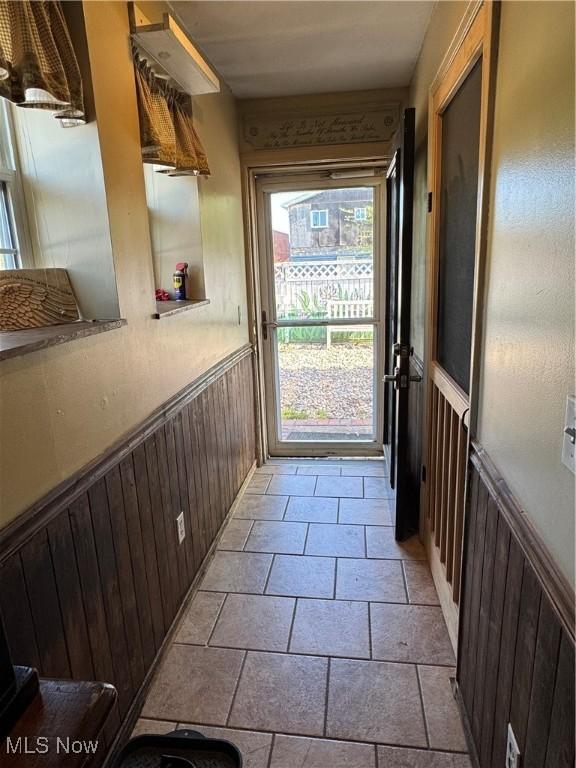 doorway to outside featuring stone finish flooring and wainscoting