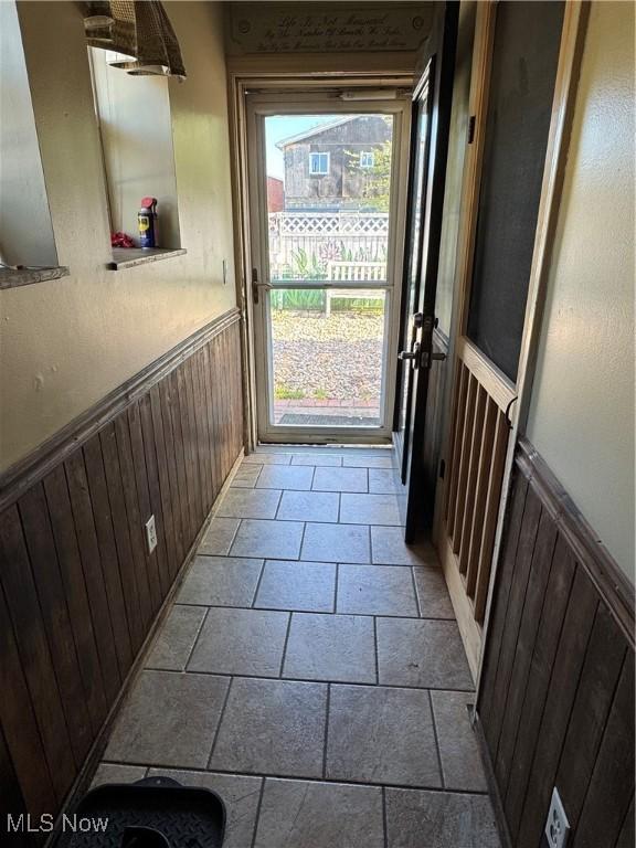 doorway with wainscoting, wooden walls, and stone tile flooring