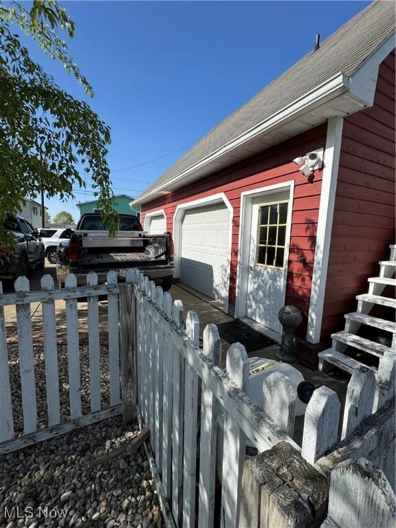 view of property exterior with fence, an outdoor structure, a shingled roof, and a garage