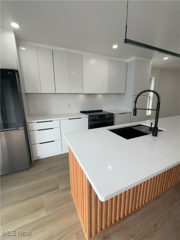 kitchen with a sink, modern cabinets, stainless steel fridge, black electric range oven, and light countertops
