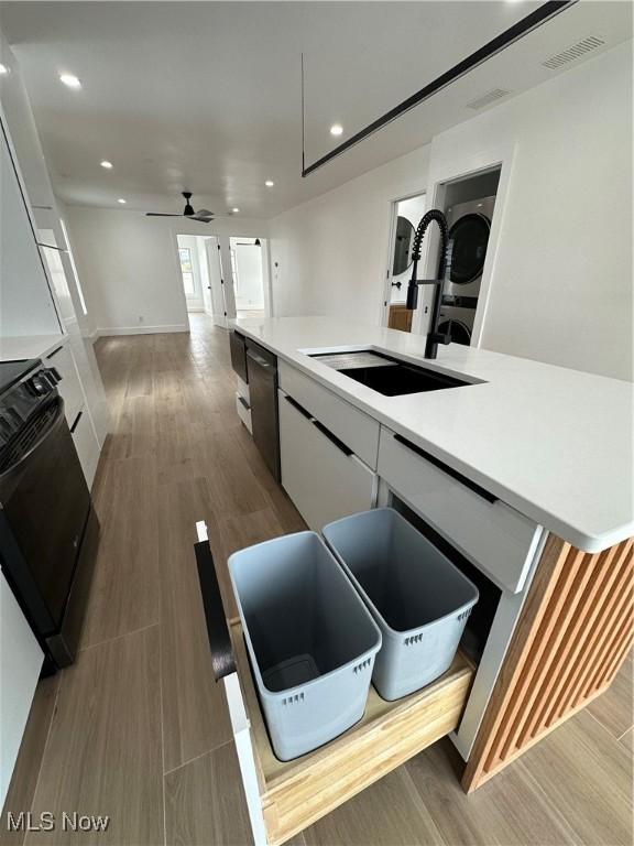 kitchen featuring range, a sink, stacked washer / drying machine, visible vents, and light countertops