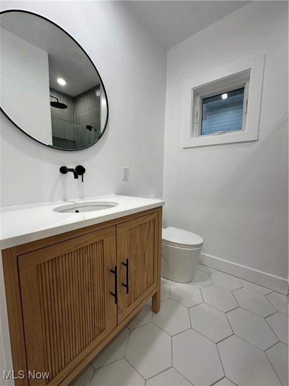 bathroom featuring toilet, walk in shower, vanity, and baseboards