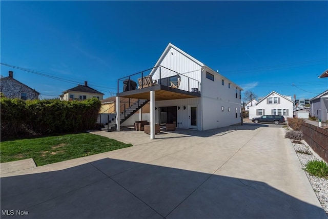 rear view of property with a patio area, fence, board and batten siding, and stairs