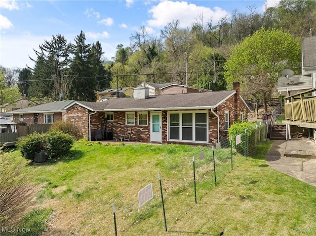 view of front of property featuring a chimney, brick siding, fence, a wooden deck, and a front lawn