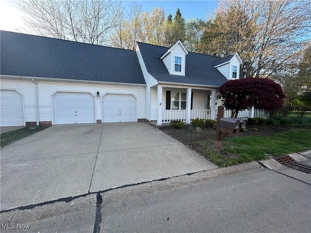 new england style home featuring concrete driveway, a garage, covered porch, and a shingled roof
