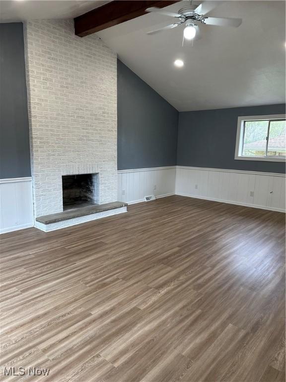 133 Bass Dr, Weirton, WV 26062 - unfurnished living room with a brick fireplace, wood finished floors, ceiling fan, vaulted ceiling with beams, and a wainscoted wall