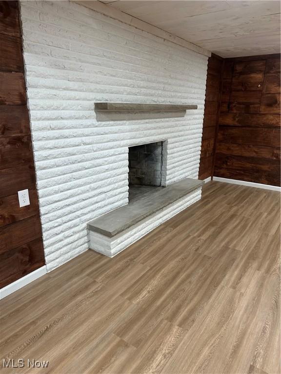 133 Bass Dr, Weirton, WV 26062 - unfurnished living room featuring baseboards, a brick fireplace, wood walls, and wood finished floors